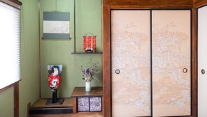 A traditional Japanese room with tatami flooring, a shoji screen door, a hanging scroll, and a small shrine table with a statue and flowers. - Karakara (Osaka)