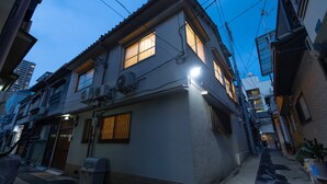 A narrow urban street with a two-story building featuring a small front porch and a visible air conditioning unit. - Karakara (Osaka)