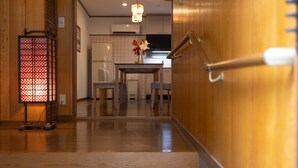 A wooden interior hallway leading to a dining area with a table and chairs, a decorative lantern, and a modern kitchen in the background. - Karakara (Osaka)