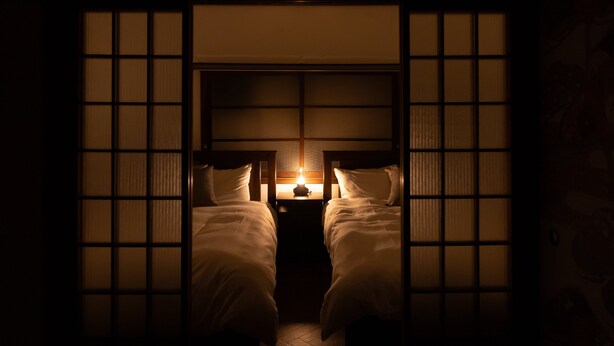 A traditional Japanese-style room with two beds, a low wooden headboard, and a small table with a lamp. - Karakara (Osaka)
