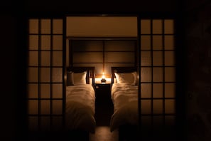 A traditional Japanese-style room with two beds, a low wooden headboard, and a small table with a lamp. - Karakara (Osaka)
