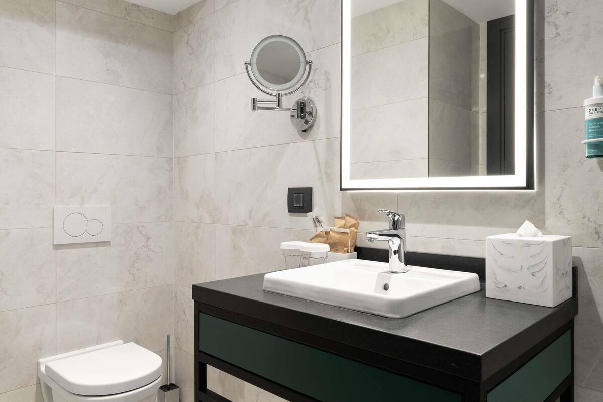 A modern bathroom with a toilet, sink, mirror, and hand soap dispenser.