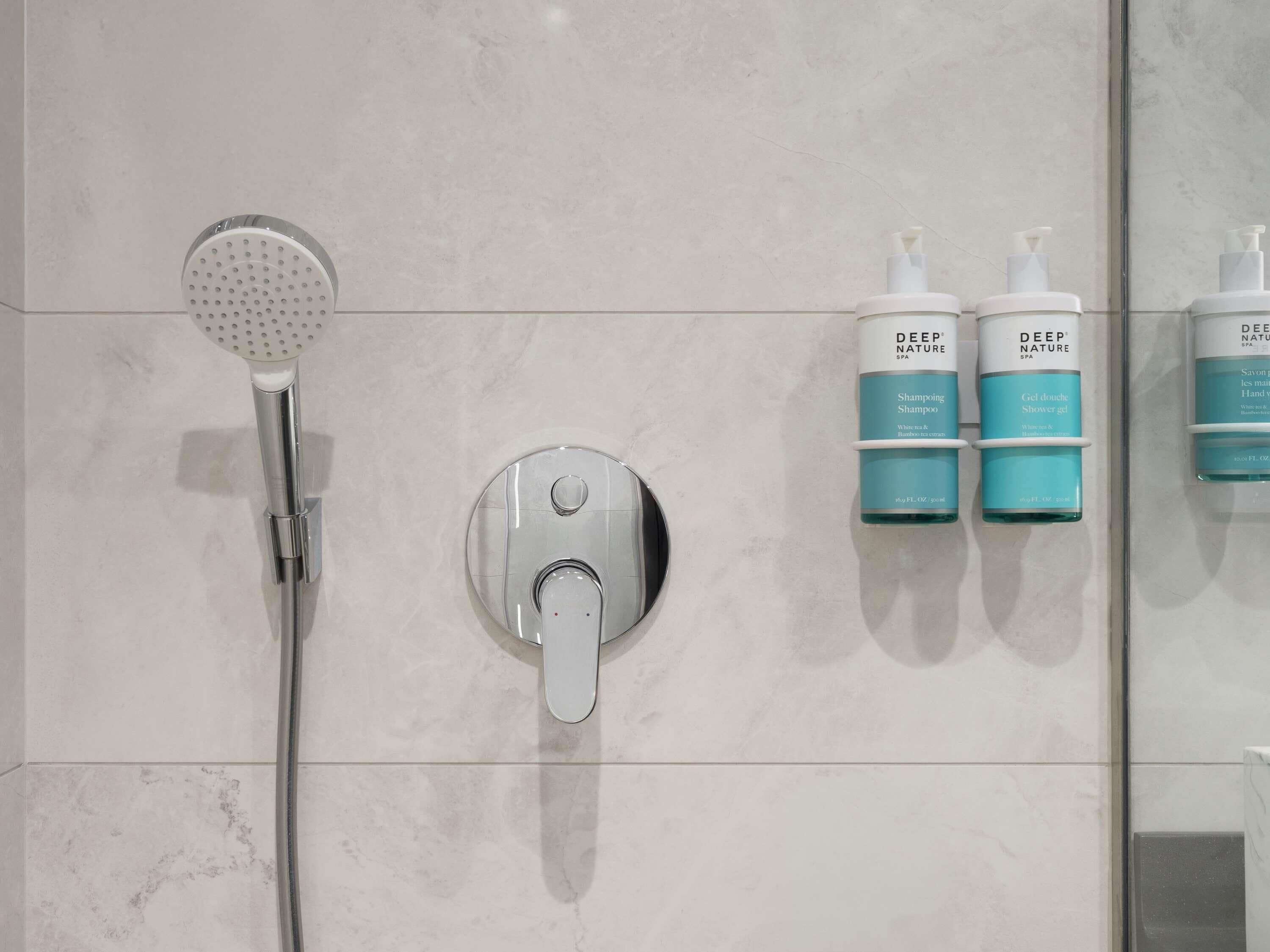 Un baño con ducha, un grifo de pared y dos botellas de champú y gel de ducha Deep Nature Spa.