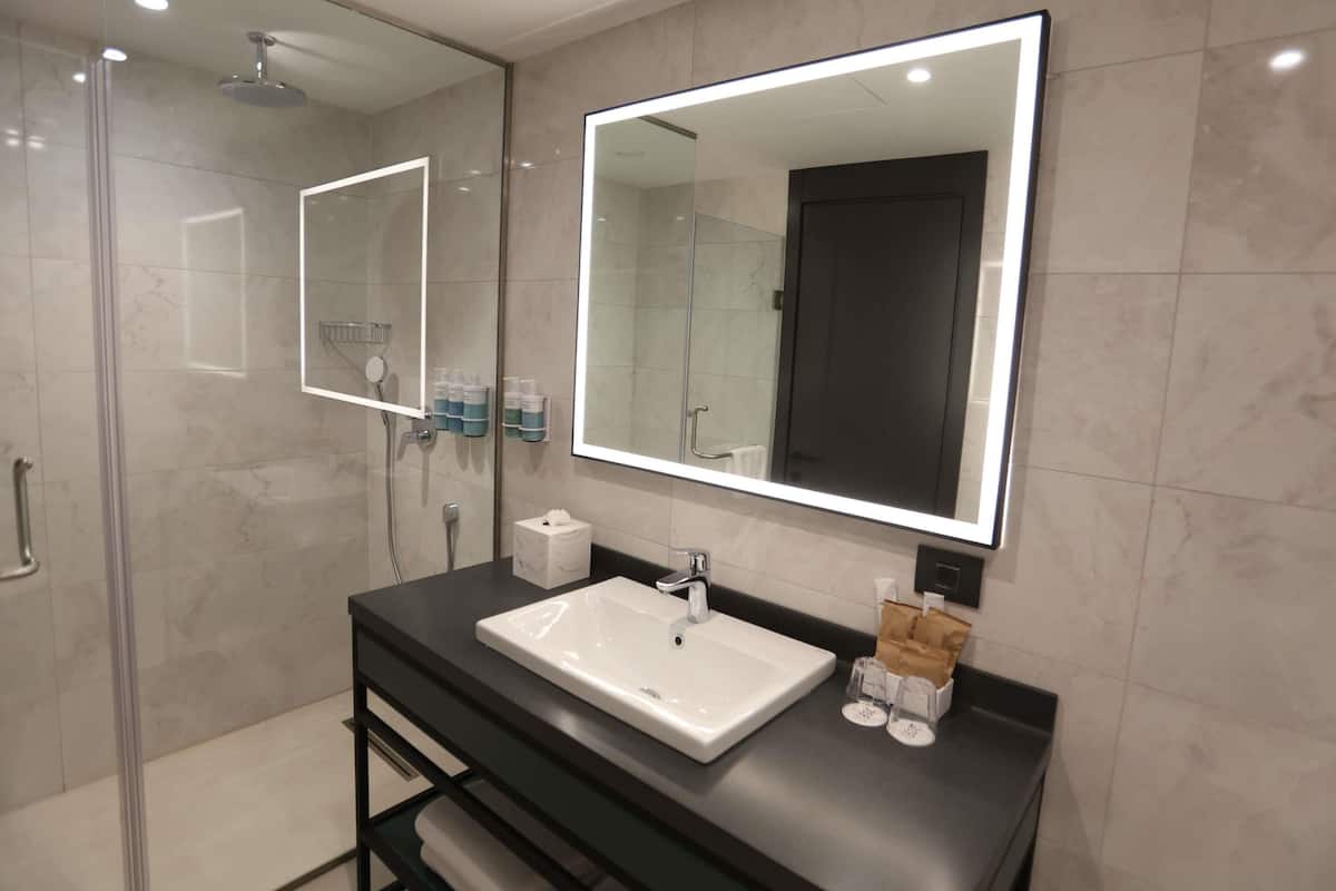 A modern bathroom with a large mirror, a white sink, and a glass shower enclosure.
