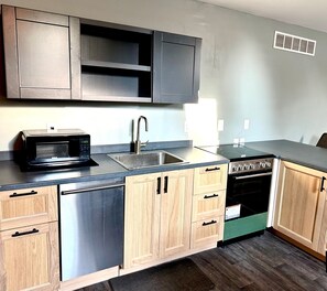 A modern kitchen with stainless steel appliances, wooden cabinets, and a black countertop. - Modern Suite in Downtown Afton, 5min to skiing, hiking, riverboating & more! (Afton)