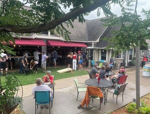 An outdoor patio area with tables and chairs, surrounded by greenery and a building with a red awning. - Modern Suite in Downtown Afton, 5min to skiing, hiking, riverboating & more! (Afton)