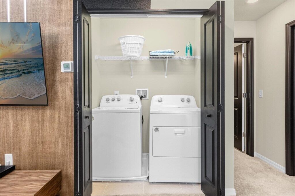 Une buanderie équipée de deux machines à laver et de deux sèche-linge à chargement frontal, d’un mur en bois, d’une étagère avec des paniers à linge et d’un tableau encadré.