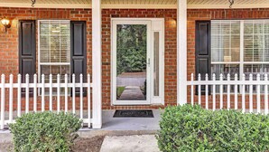 A brick house with a white picket fence, a welcome mat, and a door with a view of a road and trees. - Soothing Savannah Townhome with Patio! (Savannah)
