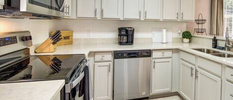 A modern kitchen with white cabinets, stainless steel appliances, and a black countertop.