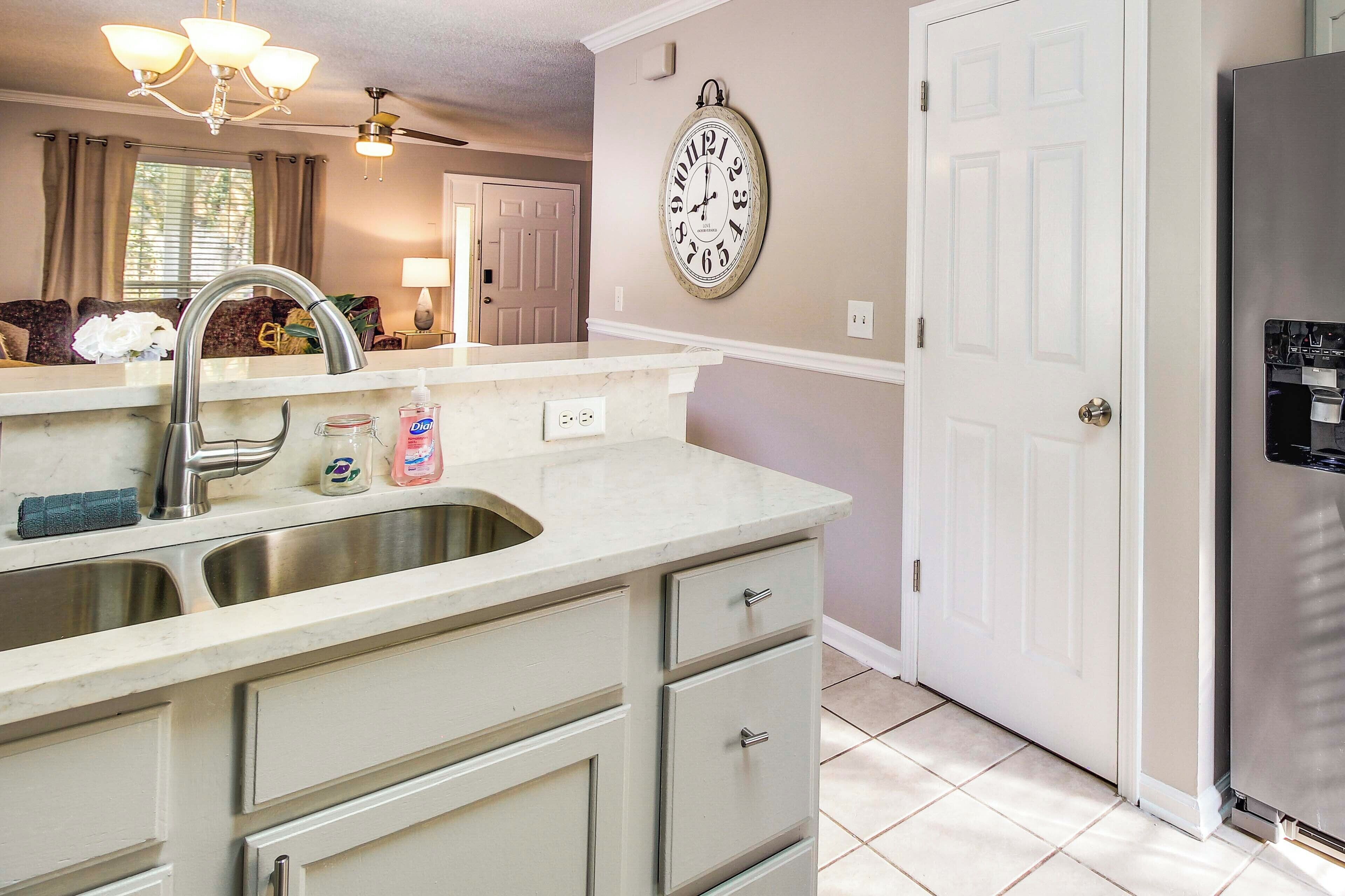 A kitchen with a double sink, a refrigerator, and a wall clock.