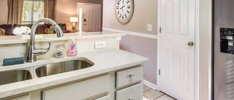 A kitchen with a double sink, a refrigerator, and a wall clock.
