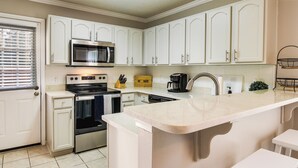 A kitchen with white cabinets, a microwave, an oven, a coffee maker, and a sink. - Soothing Savannah Townhome with Patio! (Savannah)