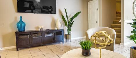 A living room with a dark wood cabinet, a round marble coffee table, a large potted plant, and a modern abstract sculpture.