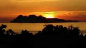 Ein Sonnenuntergang über einem Gewässer, mit verschwommenen Silhouetten von Land und Bäumen.