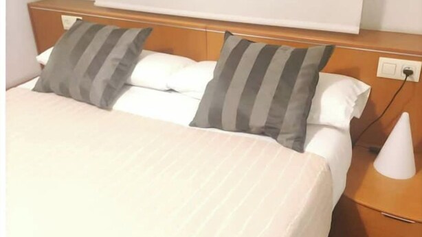 Ein Hotelzimmer mit Bett, zwei Kissen, einem Nachttisch und einer Lampe.
