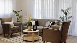 Una sala de estar con un sofá, dos sillones, una mesa de centro y plantas en macetas.