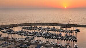 Un puerto deportivo con barcos amarrados, un muelle que se adentra en el agua y un atardecer de fondo.