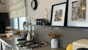 Una cocina moderna con estufa a gas, microondas y pileta. Hay cuadros en la pared y una ventana con persianas.
