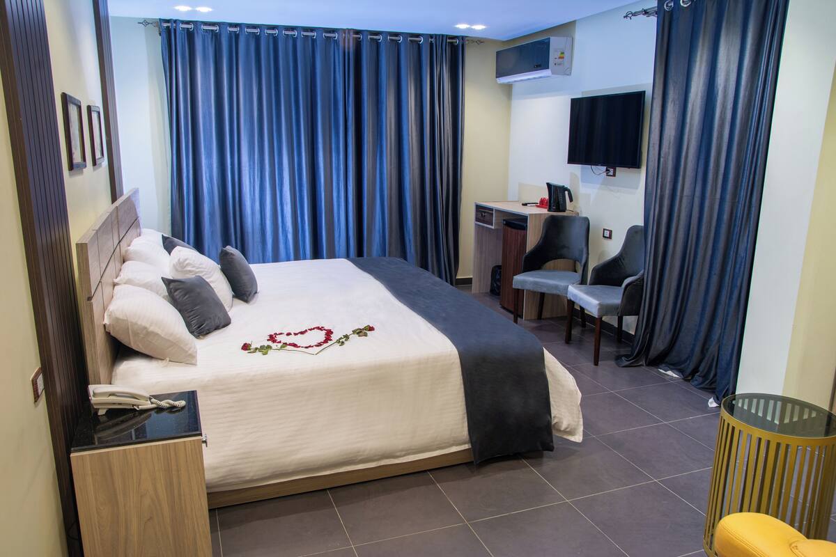 Una habitación de hotel con cama, escritorio, silla, televisor y un cesto de basura.