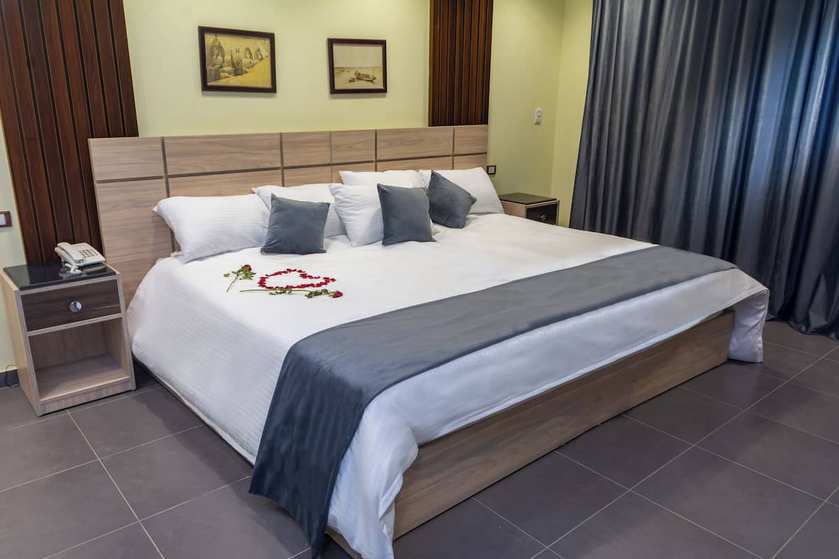 Una cama bien hecha con cabecera de madera, una mesita de noche con un teléfono y una mesita con una lámpara.