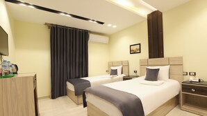 Een hotelkamer met twee bedden, een bureau, een kledingkast en een airconditioning.