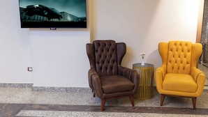 Een hal met een wandgemonteerde flatscreen-tv, twee gestoffeerde fauteuils, een bijzettafeltje met een vaas, en een kamer met een patroon.