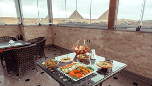 Un coin repas avec une table en verre préparée pour le repas, des chaises en osier et une vue sur les pyramides.