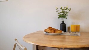 A round wooden table with a plate of croissants, a vase with green plants, and two glasses of orange juice. - Butterfly Gardens (Woodville)