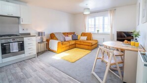 A modern kitchen with a built-in oven, a dining area with a wooden table and chairs, and a cozy living space with a sofa and a yellow rug. - Butterfly Gardens (Woodville)