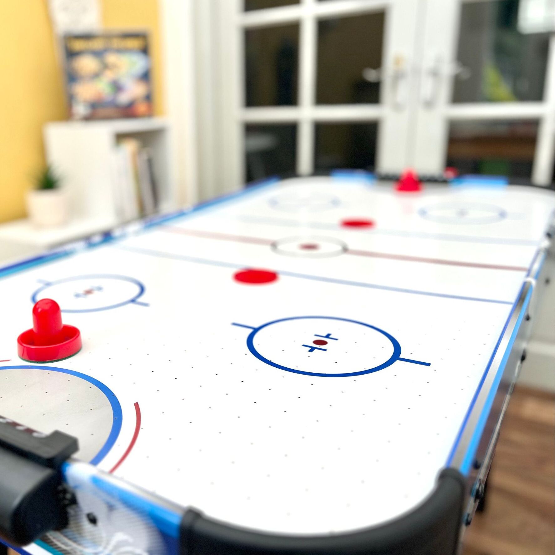 A close-up of an indoor table hockey game with a white table, blue and red puck holders, and a hockey puck.
