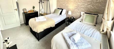 A bedroom with two beds, a bedside table, a nightstand, a mirror, a clock, and a wall-mounted fan.