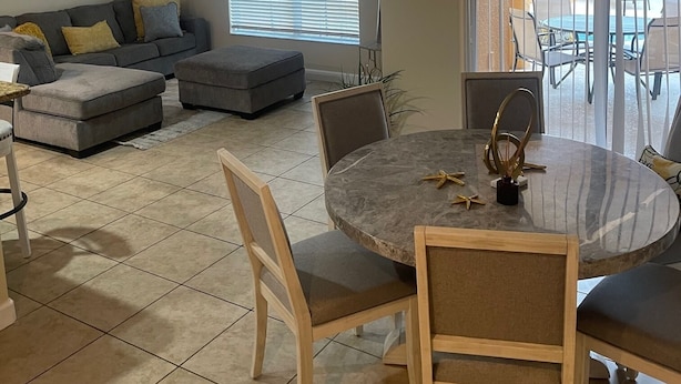 Et spiseområde med et rundt bord, stole, en grå sofa og en loftsvifte.