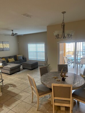 A dining area with a round table and chairs, a gray sofa, and a ceiling fan. - BEAUTIFUL HOME 7 MINS FROM DISNEY, UNIVERSAL NEAR DINING AND SHOPPING (Kissimmee)