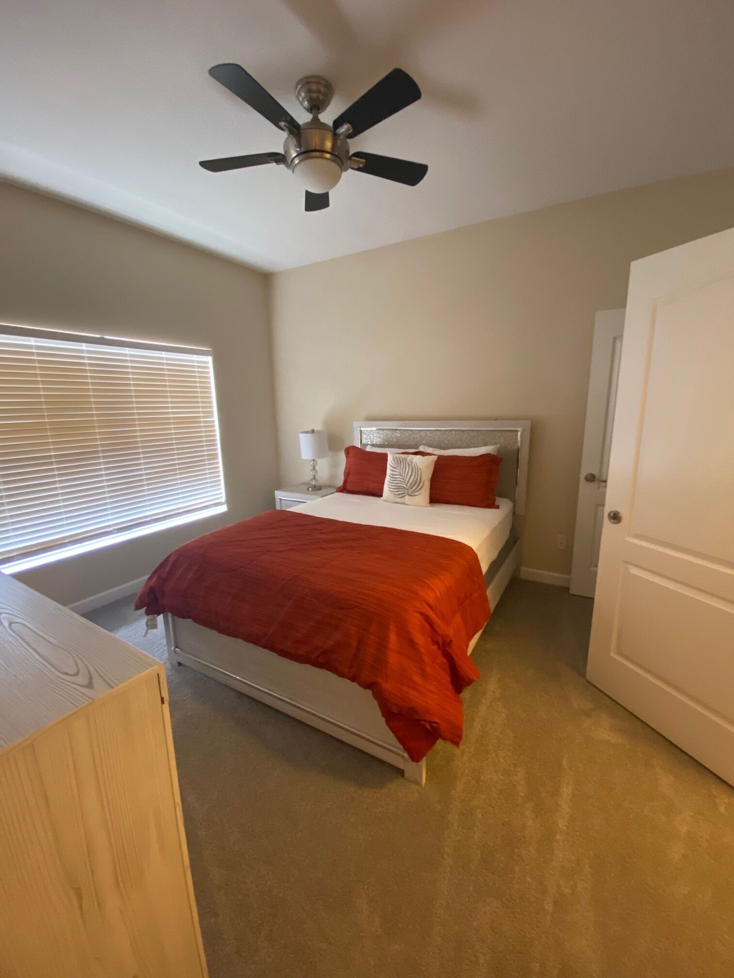 Un dormitorio con cama, mesita de noche, ventilador de techo y ventana con persianas.