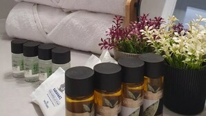 Ein Badezimmer mit ordentlich gestapelten weißen Handtüchern, einem Spiegel und verschiedenen Pflegeprodukten, darunter Hautpflegeartikel sowie einer Pflanze mit Blüten.