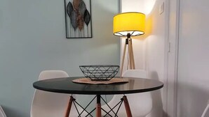 Ein Essbereich mit einem runden Tisch, weißen Stühlen, einer gelben Stehlampe und einem gerahmten Kunstwerk an der Wand.