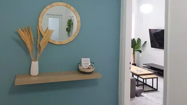 Ein Flur mit türkisfarbenen Wänden, einem Holzbodenregal mit Spiegel, einer kleinen Pflanze und einem Willkommensschild.