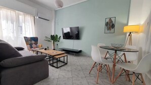 Ein modernes Wohnzimmer mit einer Couch, einem Couchtisch, einem Fernseher und einem Essbereich mit Stühlen und einer Lampe.
