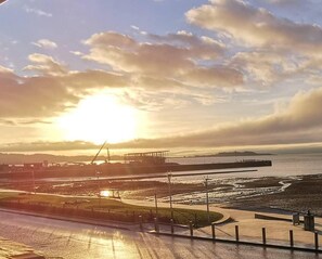 A waterfront view with a sunset, a pier, and a construction site in the background. - Fantastic 2 Bedroom, Spacious and Great Location! (Helensburgh)