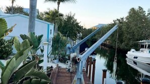 A dock with a boat, palm trees, and a building in the background. - Boater’s Paradise: 3BR Canal Front Home + Fish Cleaning Station (Big Pine Key)