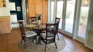 A dining area with a round glass table, four wicker chairs, and a woven rug. - Boater’s Paradise: 3BR Canal Front Home + Fish Cleaning Station (Big Pine Key)