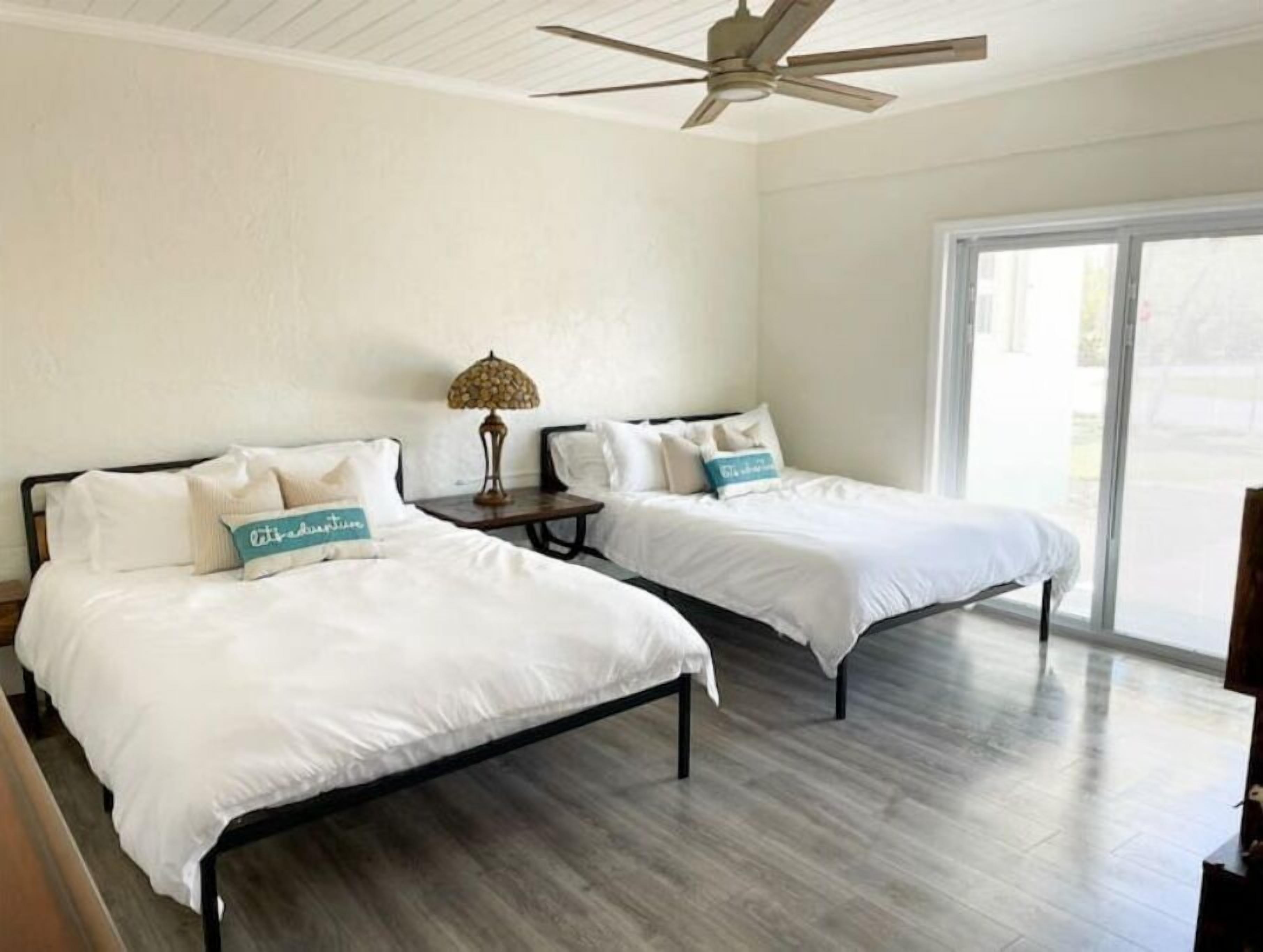 A hotel room with two beds, a ceiling fan, and a large window.