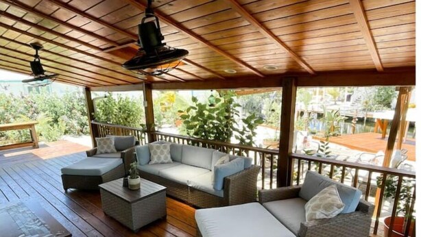 An outdoor covered patio with wicker furniture, a wooden table, and ceiling fans. - Boater’s Paradise: 3BR Canal Front Home + Fish Cleaning Station (Big Pine Key)