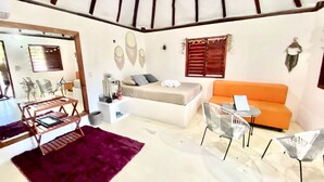 A modern living room with a white sofa, an orange couch, and a small round table. There are two chairs, a purple rug, and a wooden coffee table. - Cabañas Manati (Isla Holbox)