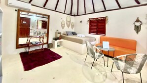 A room with a ceiling fan, a sofa, two chairs, a small table, a mirror, and a window with shutters. - Cabañas Manati (Isla Holbox)