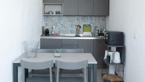 A compact kitchen with grey cabinets, a tiled backsplash, and a small dining area with two chairs and a table. - Gassa d’Amante (Castellammare del Golfo)