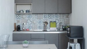 A modern kitchen with grey cabinets, a patterned backsplash, and a small dining area with a table and chairs. - Gassa d’Amante (Castellammare del Golfo)