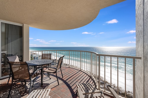 A balcony with a table and chairs, overlooking a beach with a clear view of the ocean.