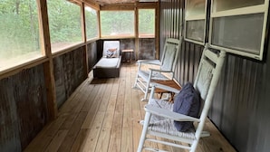 Une pièce rustique en bois, avec un banc, des fauteuils à bascule, de grandes fenêtres et un ventilateur de plafond.