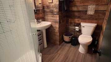 A compact bathroom with wooden walls, a white sink, a toilet, and a glass shower enclosure.